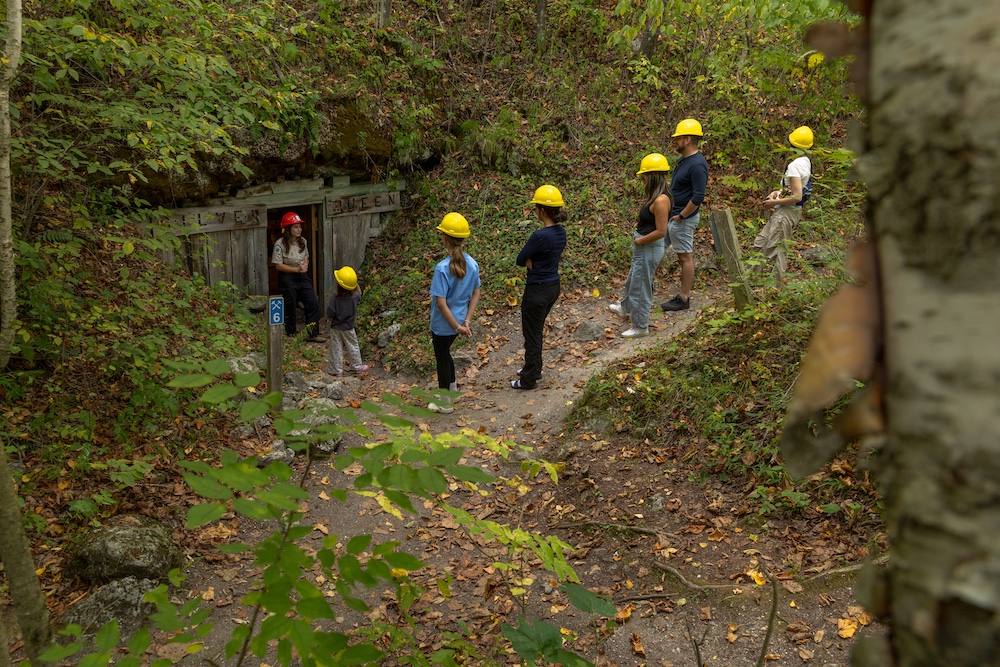 Group of people wearing yellow hard hats standing outside entrance to a mine