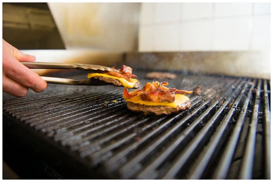 fresh burger patties topped with cheddar and bacon being taken off the grill at Burger World in North Bay.