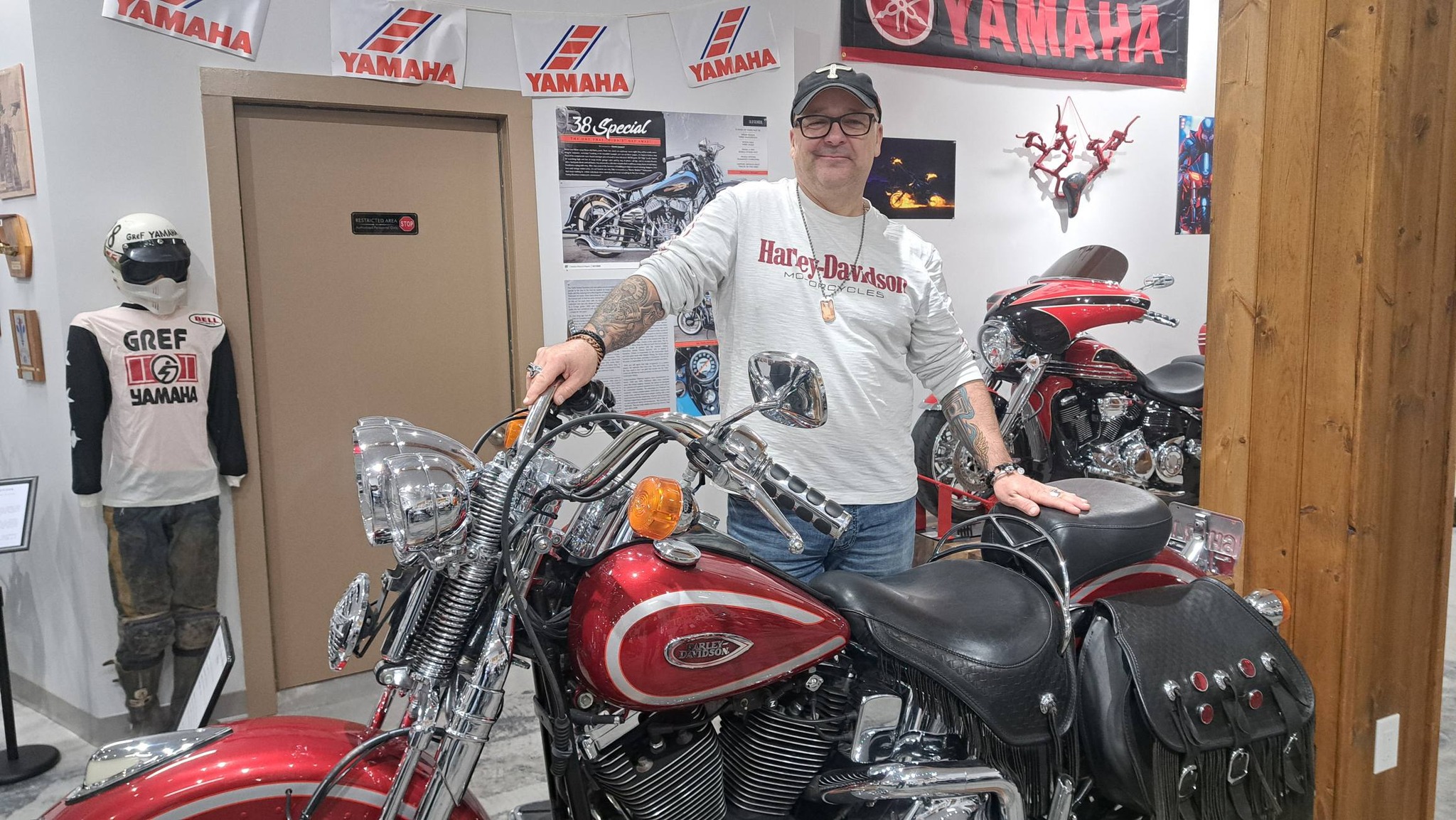 a person smiles standing next to a retro Yamaha motorcycle, surrounded by Yamaha ride gear and memorabilia at the Kisselgoff Motorcycle Museum.