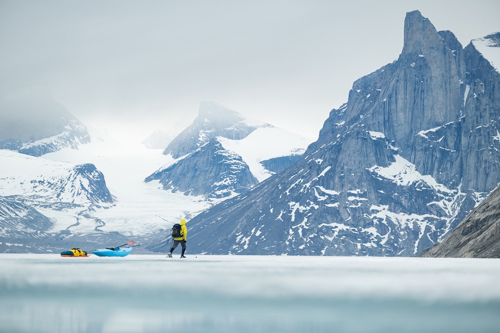 Person pulling whitewater kayak across ice with mountain in background