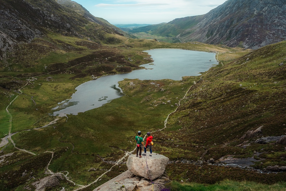 Two climbers standing at top of mountain looking down over valley