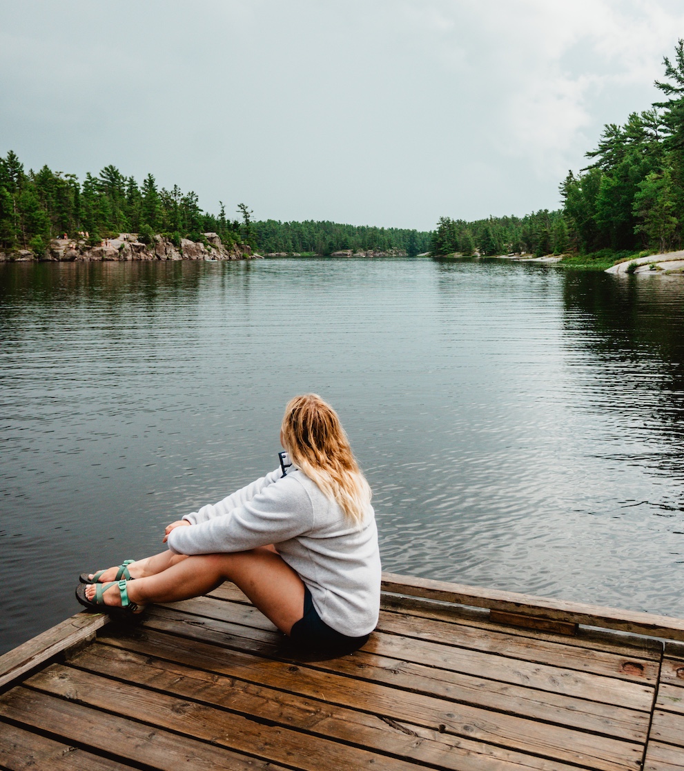 Woman sitting on edge of dock next to water