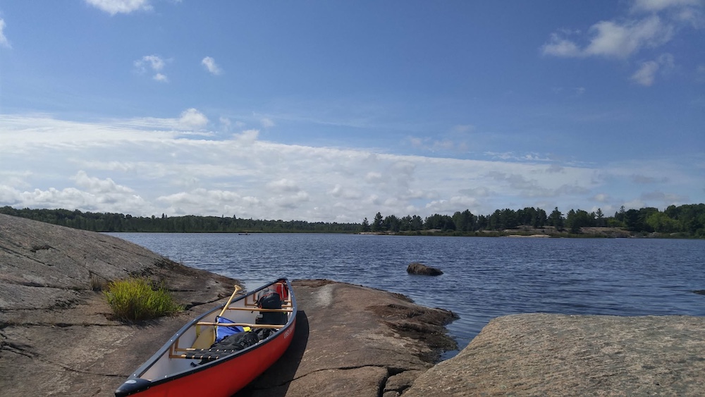 Red canoe pulled up on rocks next to lake