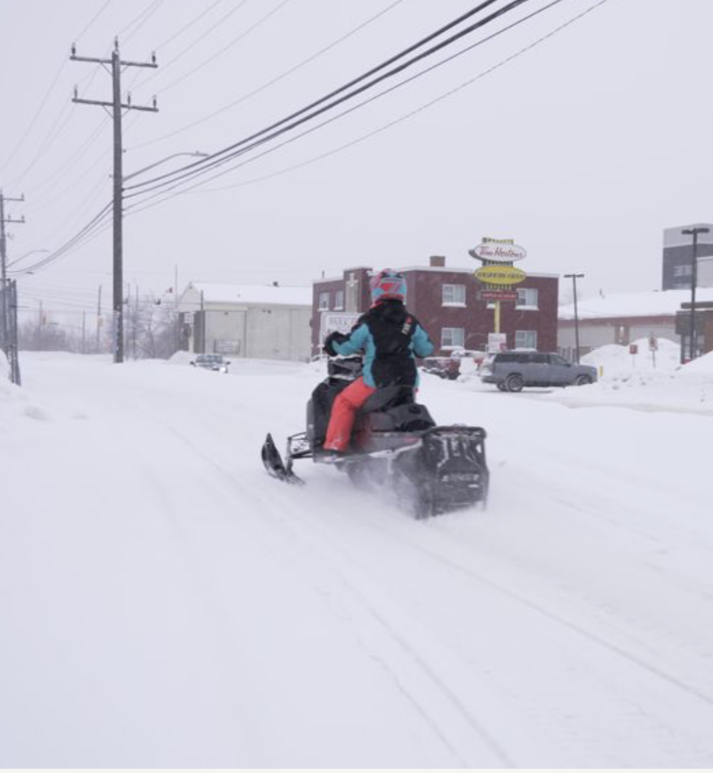 a snowmobiler rides down a snowy street past a Tim Hortons in Kaspuskasing, Ontario.