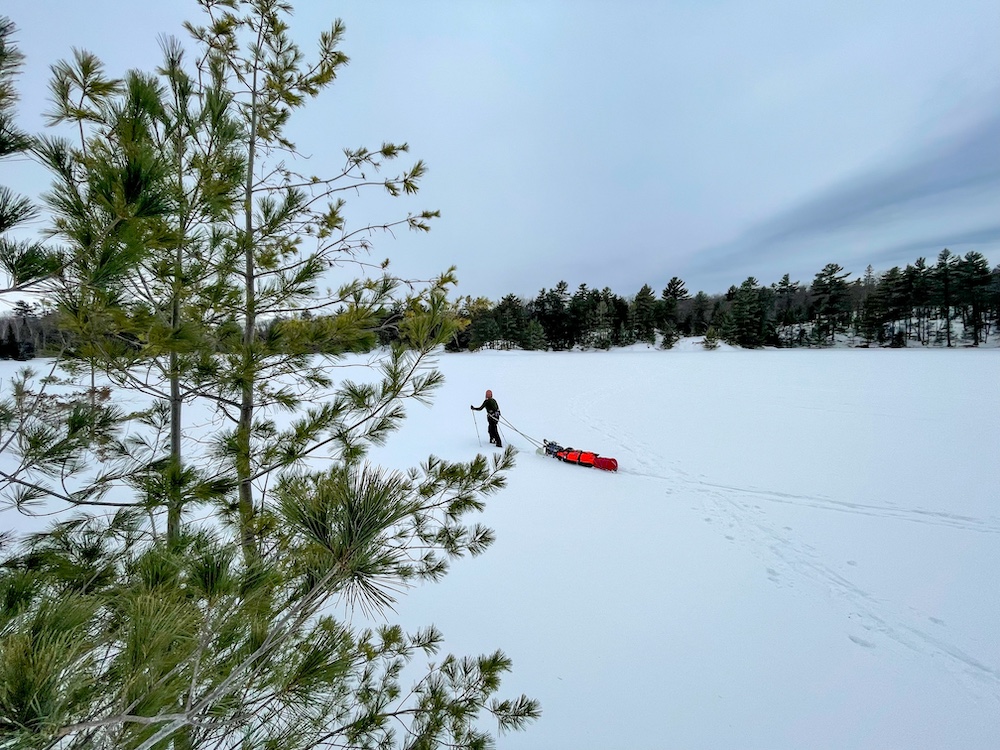 Person pulling load sled across frozen, snowy lake
