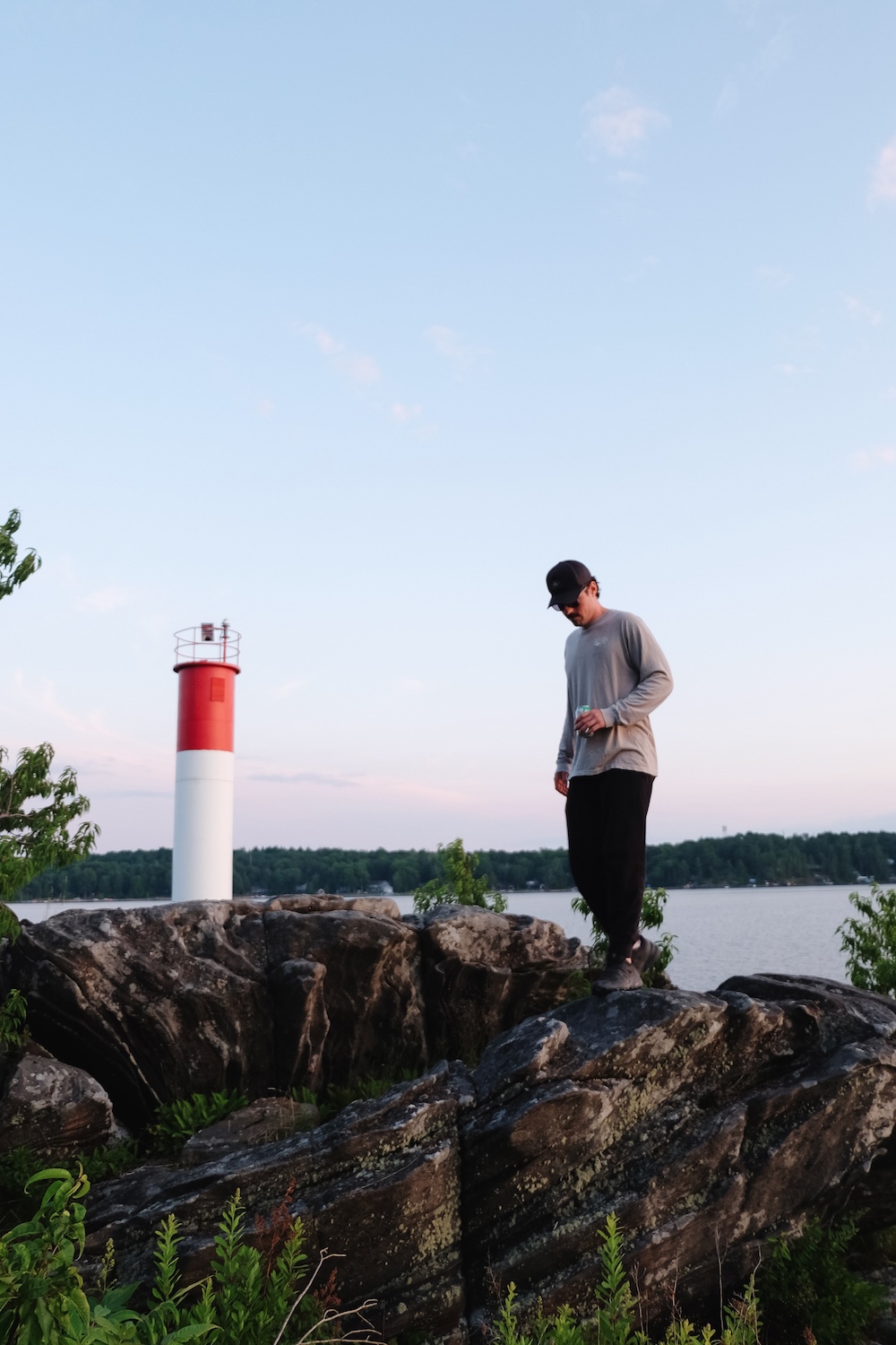 Man standing on rocks in front of red and white lighthouse