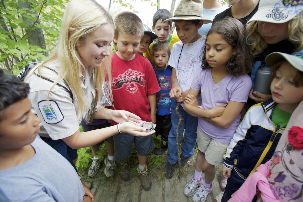 Kids gathered around a park interpreter holding a compass