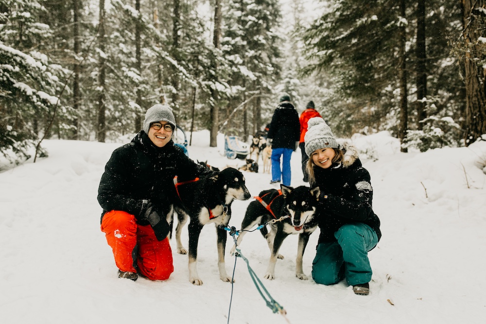 Man and woman standing with lead sled dogs in wintry woods