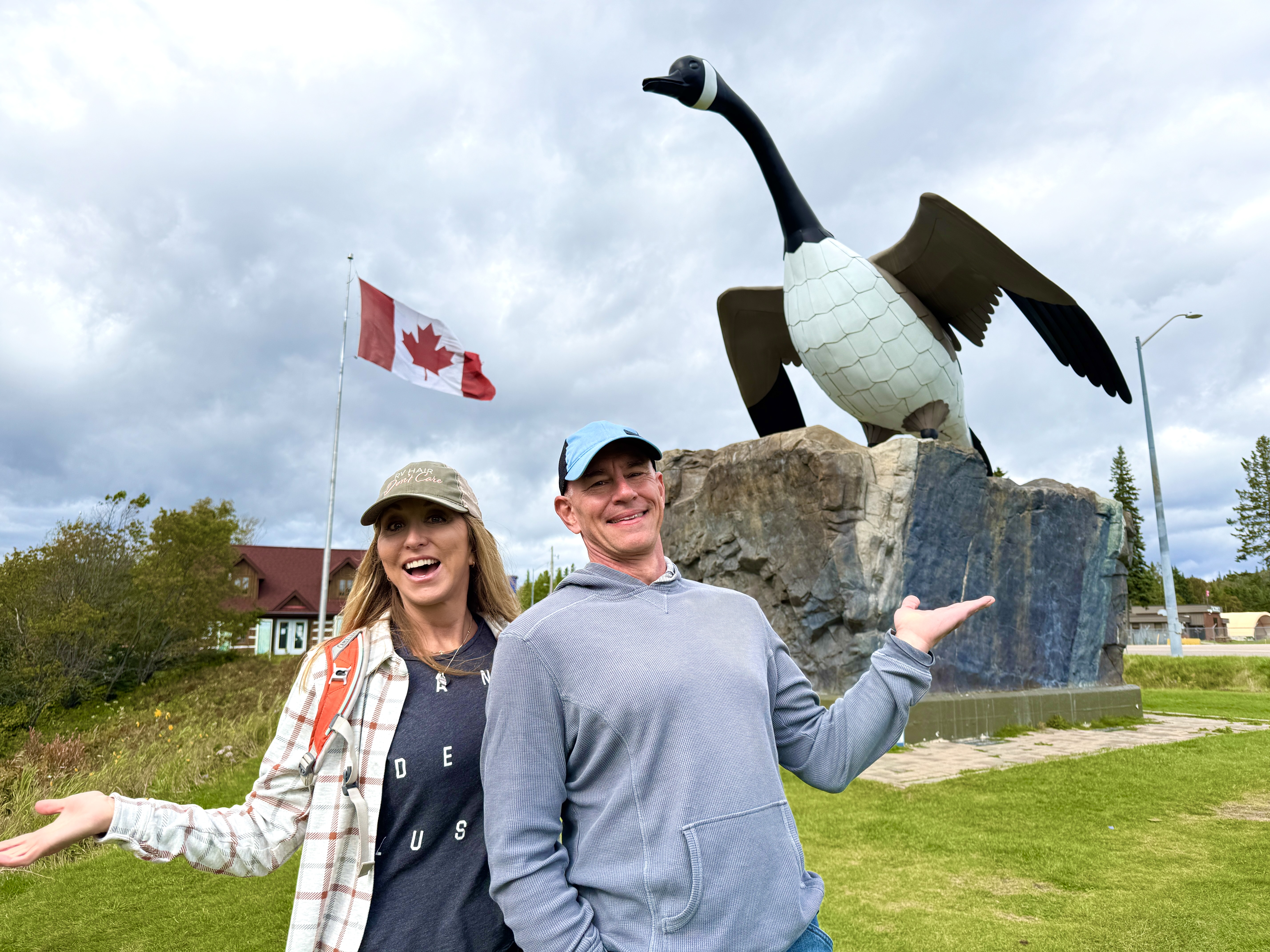 A man and a woman smile broadly as they gesture to the large Wawa Goose statue behind them. 