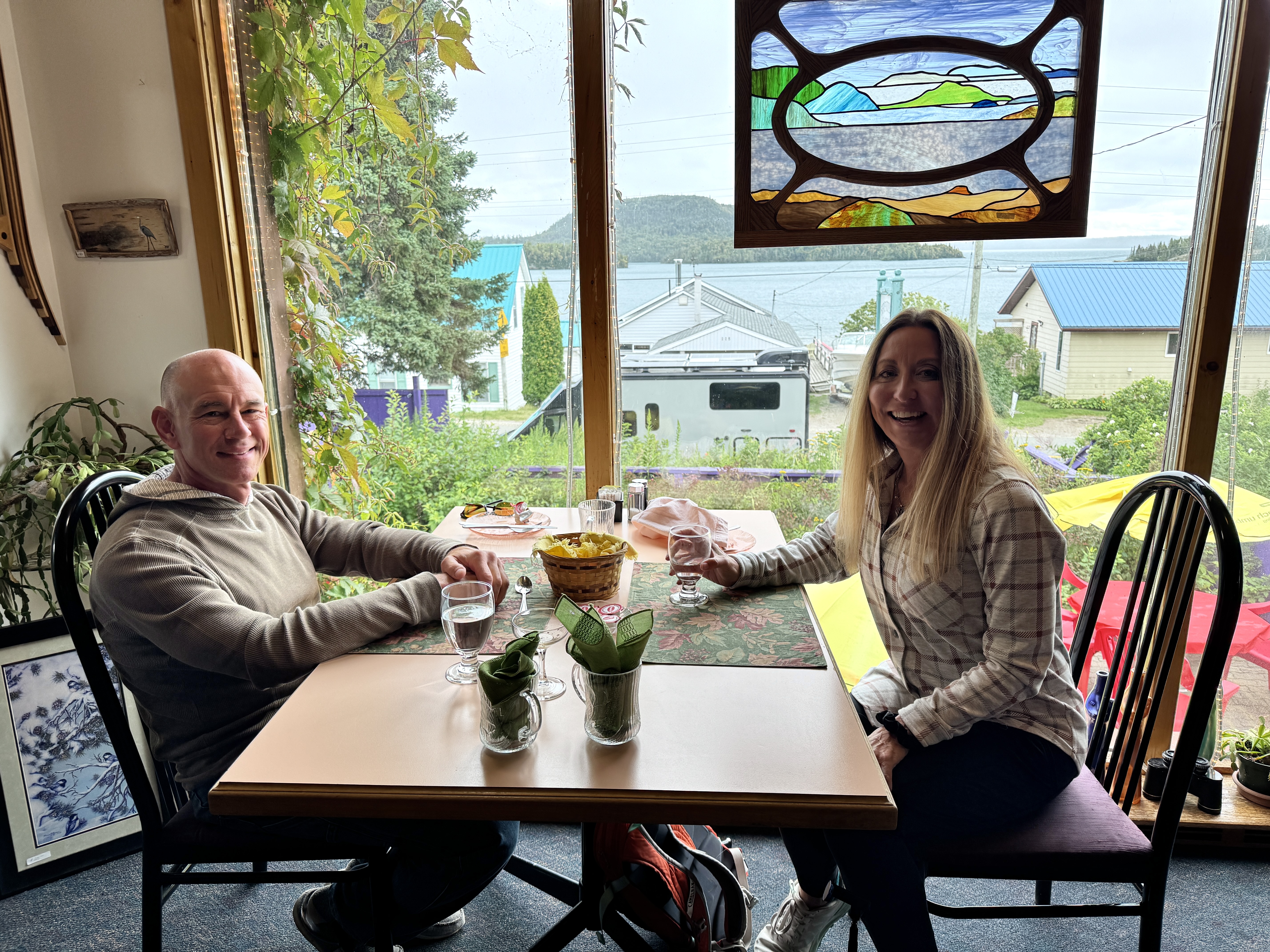 Stef and James of The Fit RV smile while sitting at a table overlooking Lake Superior at Serendipity Gardens.