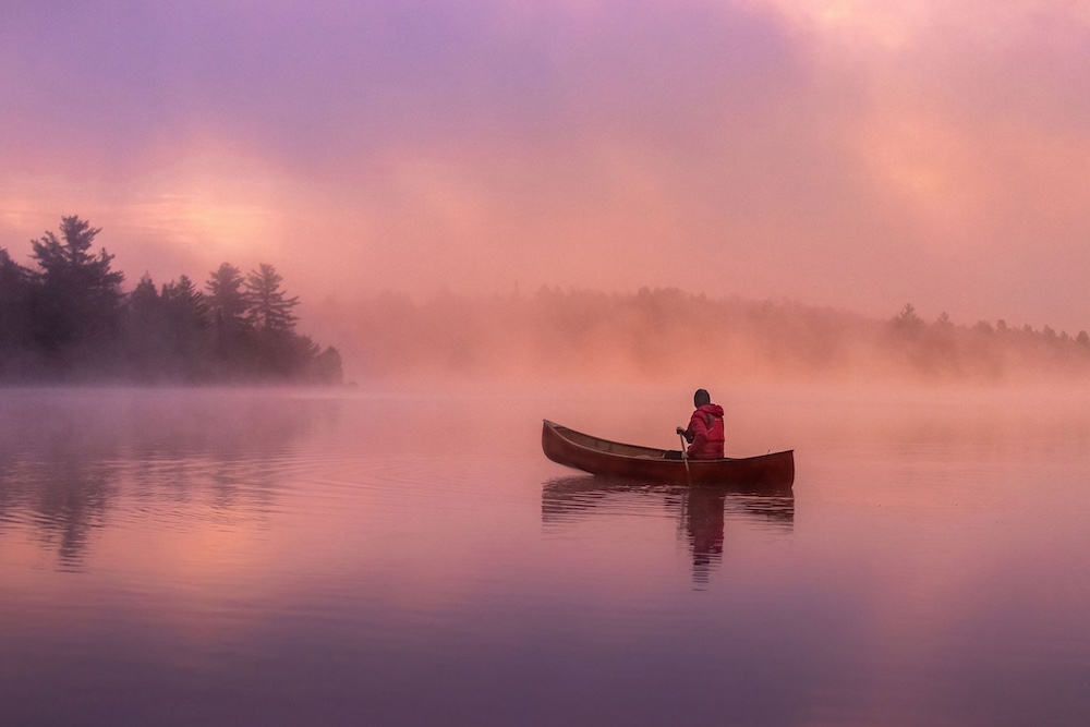 Person paddling canoe on misty morning