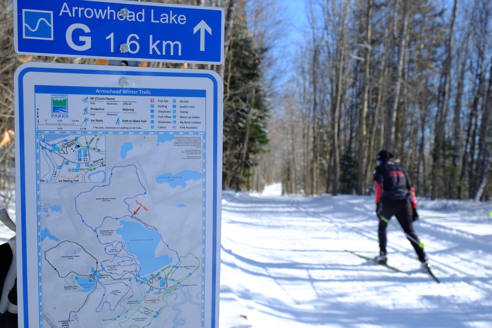 Ski trail sign with person next to it cross country skiing