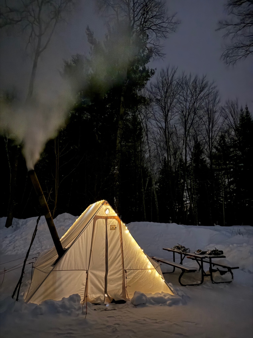 Hot tent with picnic table beside it on campsite at night