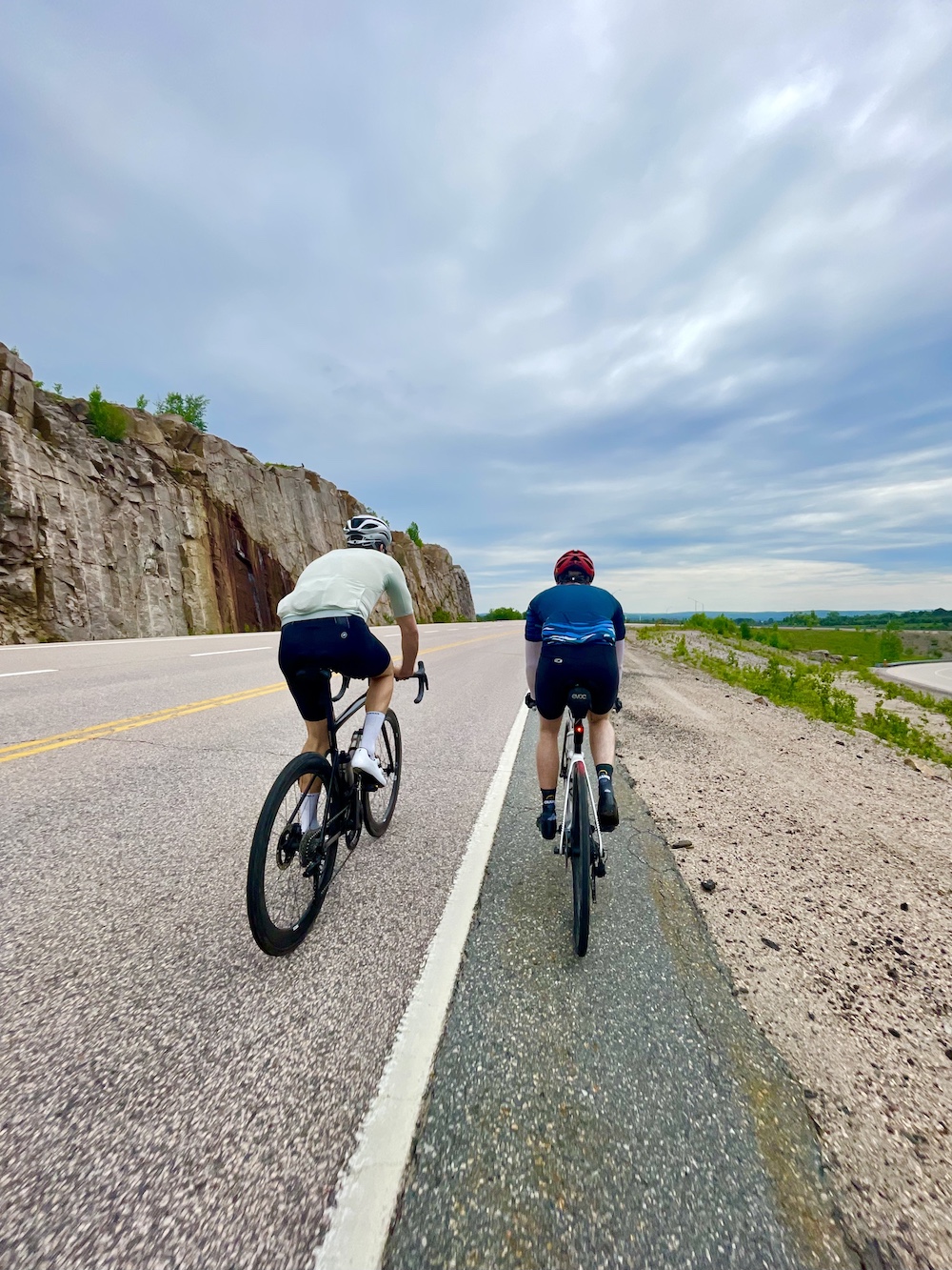 Two people on road bike near rock cut