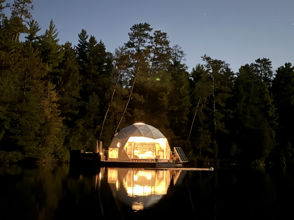 Glamping dome lit up at night on shores of lake
