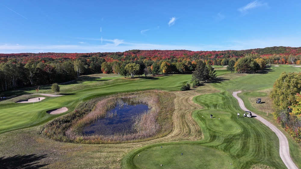 Overhead of golf course with pond and fall colours in background