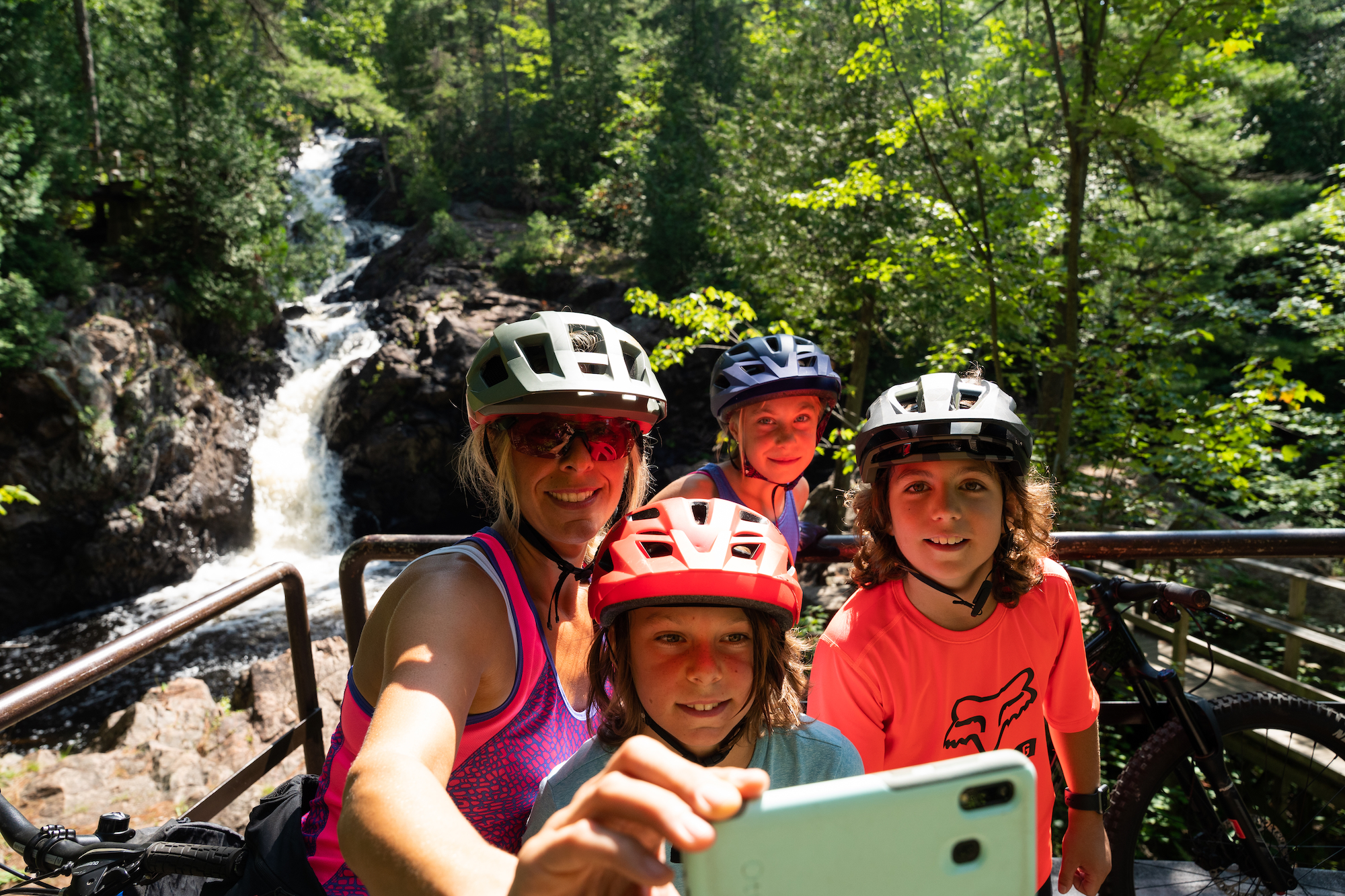 a family wearing bike helmets snaps a selfie in front of Crystal Falls on a summer day in Sault Ste. Marie. 