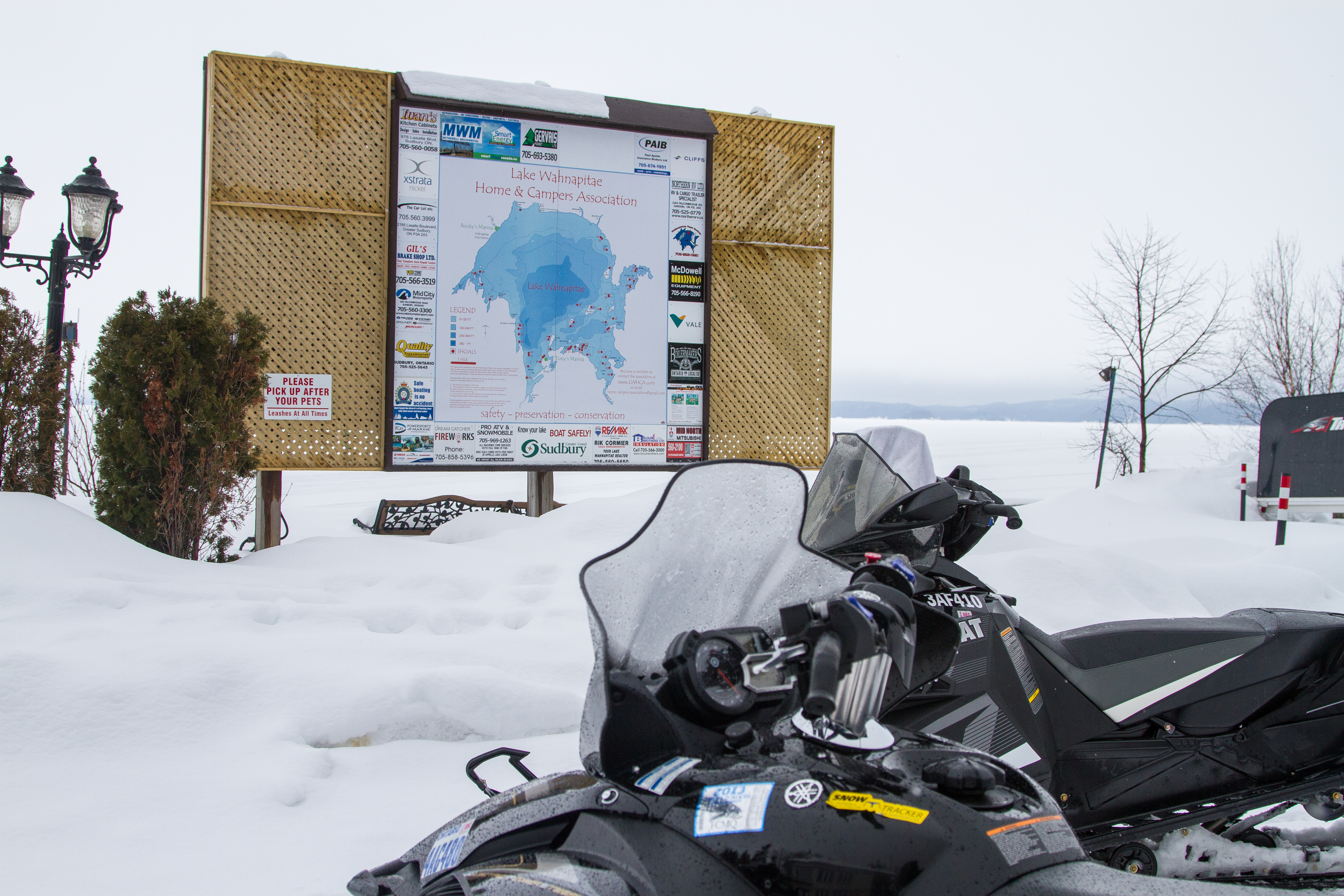 A snowmobile parked next to a wooden sign showing a map of the Chinguchi Wolf Loop.
