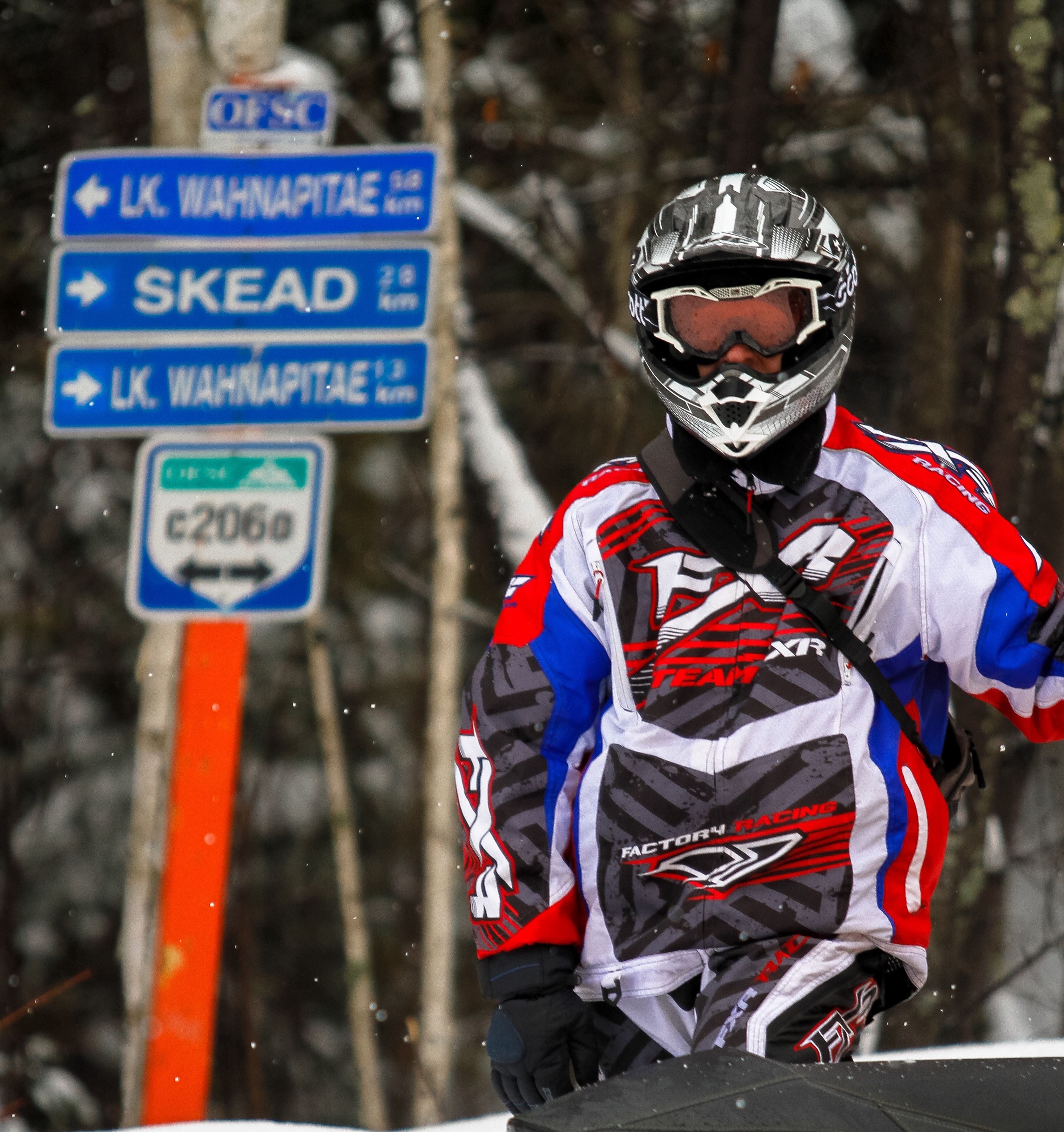 A snowmobiler in front of an OFSC trail sign marking trail c206, Skead and Lake Wahnapitae.