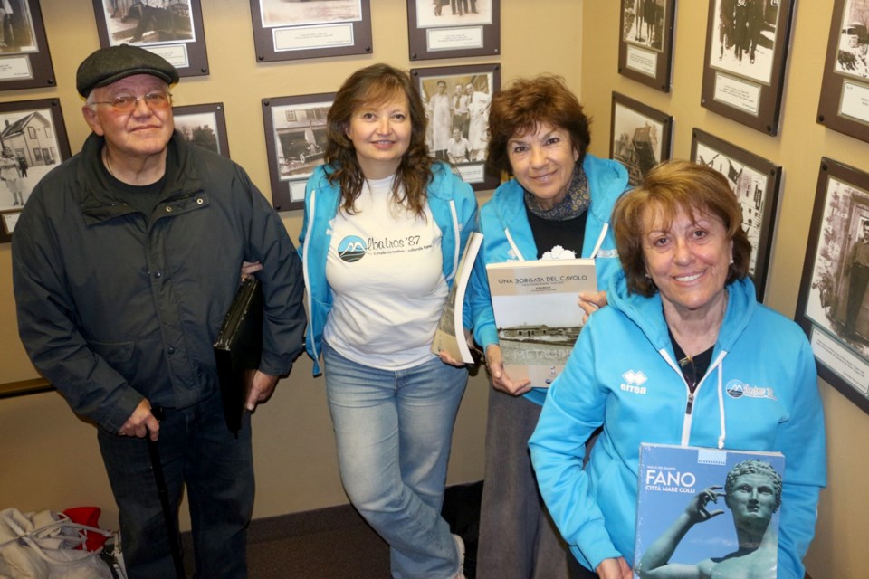 Smiling visitors from Fano, Italy standing in front of historical photos at Sudbury's Caruso Club.