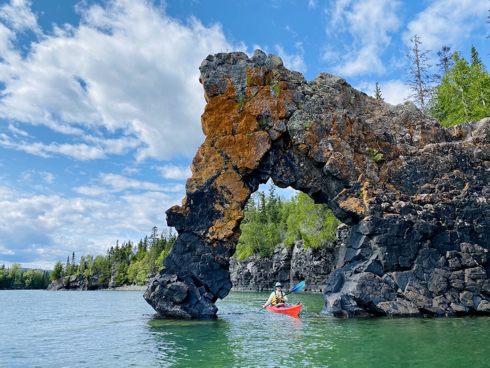 Woman paddling red kayak under arch on Lake Superior