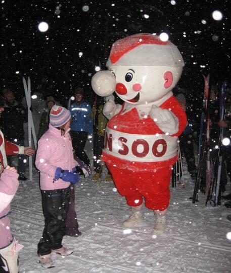 a visitor in winter clothes dances with the smiling red and white snow man mascot Mr. Bon Soo while snow falls in the evening at the Bon Soo Winter Carnival in Sault Ste. Marie. 