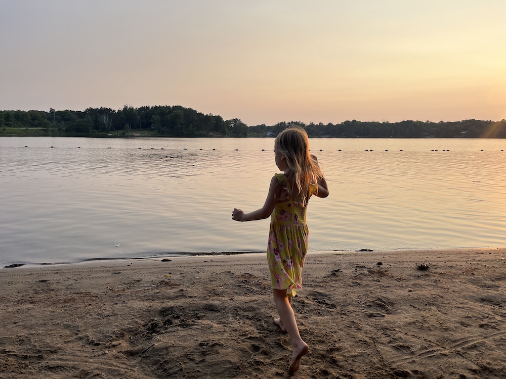 Little girl on beach next to water at sunset