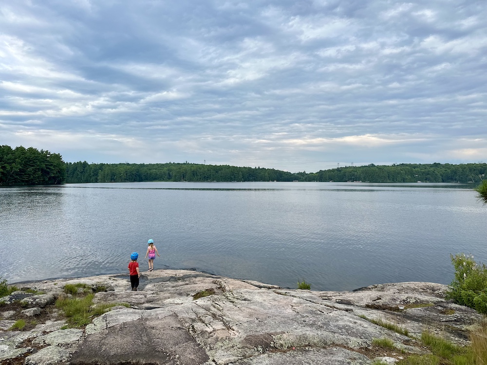 Two kids on edge of rocky shore next to lake