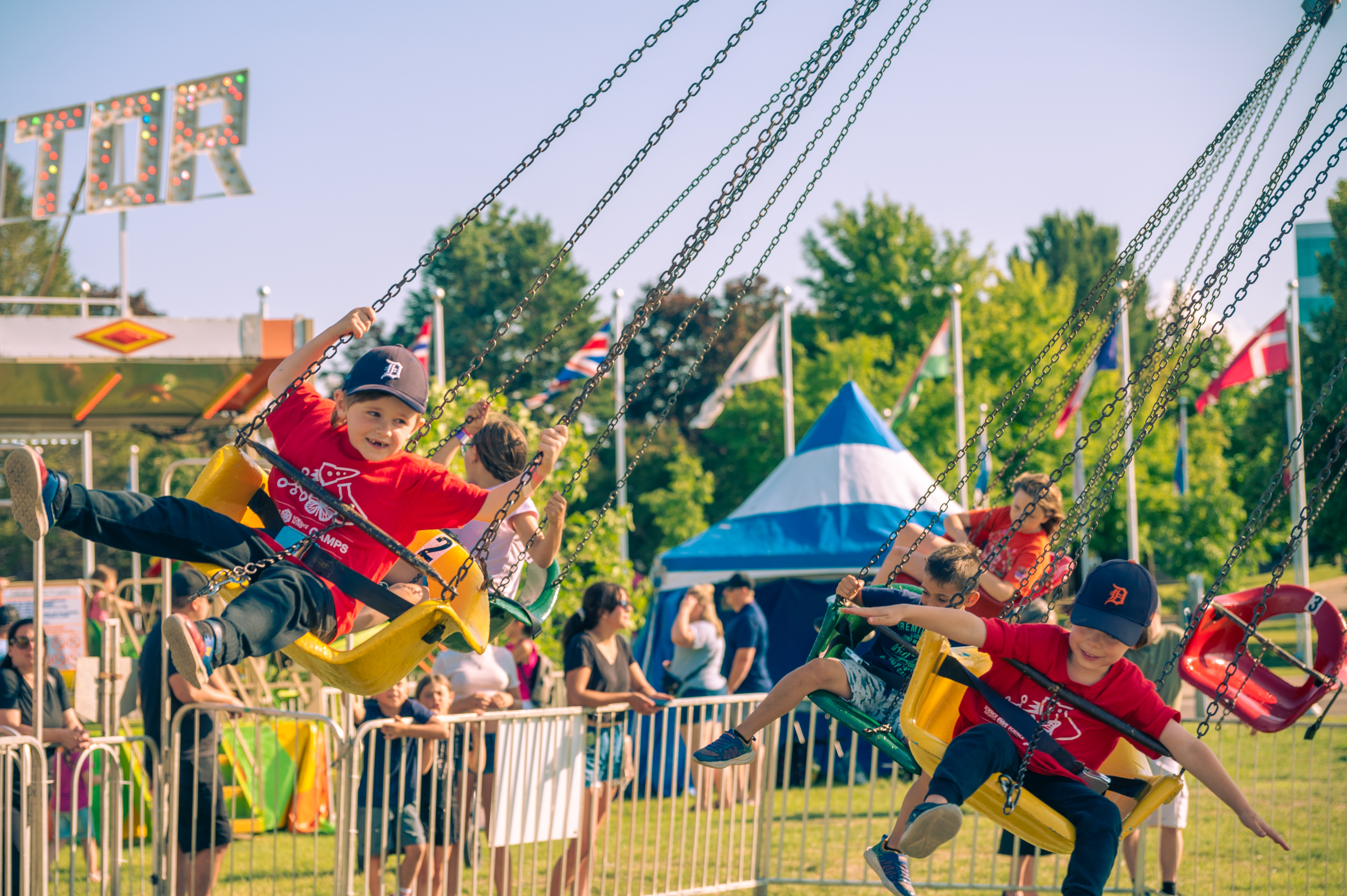 small kids smile and pretend to fly as they ride a swing ride at Rotaryfest in Sault Ste. Marie on a summer day.