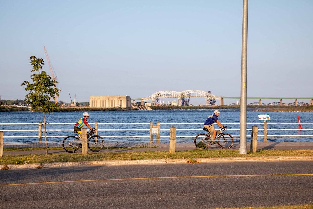 Two people cycling on paved pathway next to waterfront