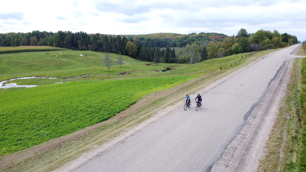 Two people cycling on paved road through farmland