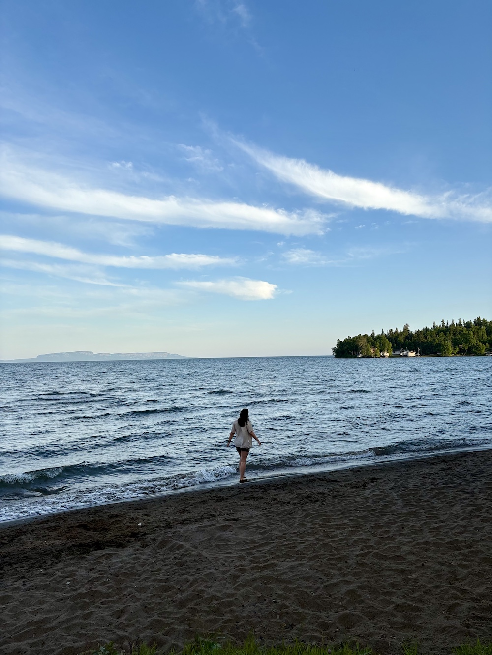 Woman walks along beach at water's edge with the shadow of the Sleeping Giant in the background
