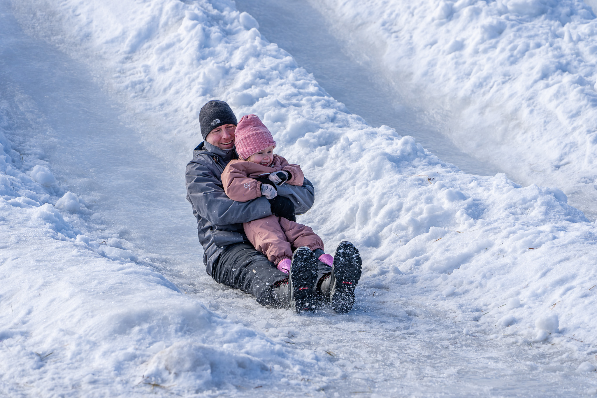 a smiling father and child slide down icy snow slides at the Bon Soo Winter Carnival. 