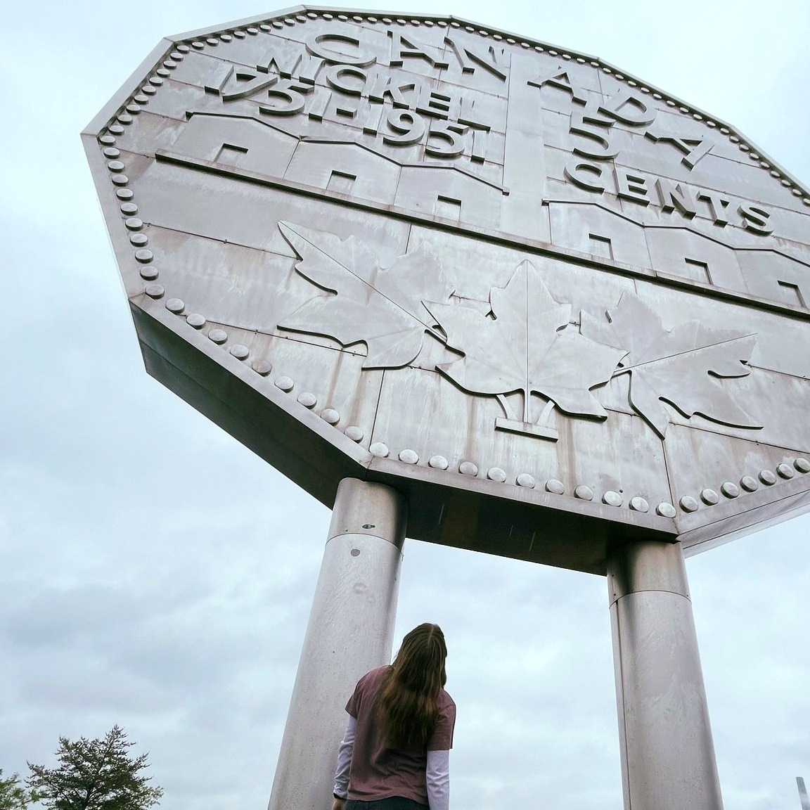 a girl cranes her neck to look up at the tall metal Sudbury Big Nickel statue looming high overhead. 