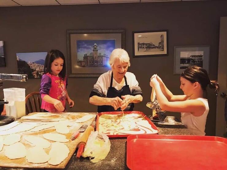 two young girls happily making pasta by hand with their grandmother as they chat.