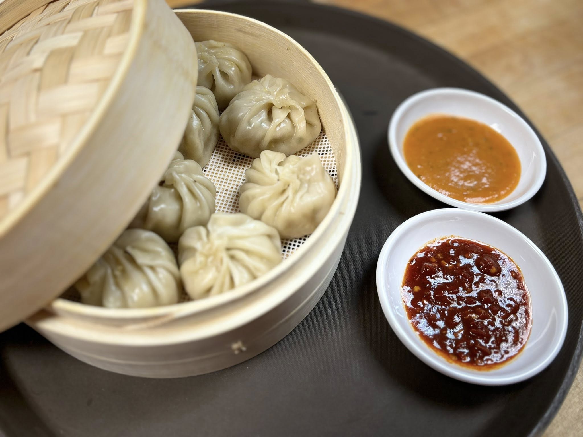 Steamed vegetable momos in a bamboo basket with chili dipping sauces on the side from Soo Spice Yeti. 