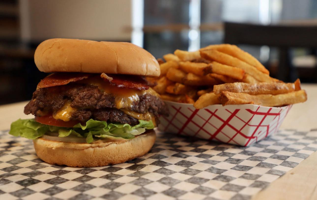 A thick burger layered with fresh lettuce, tomato and sauces on a toasted bun next to a side of fries from Stackburger. 