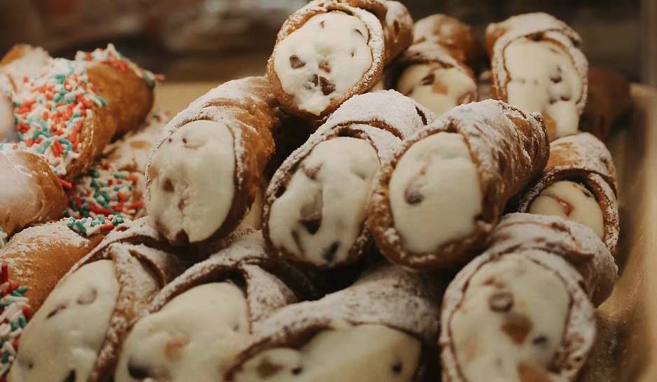 cream-filled canolli decorated with sprinkled and nuts stacked up on display and Regency Bakery.