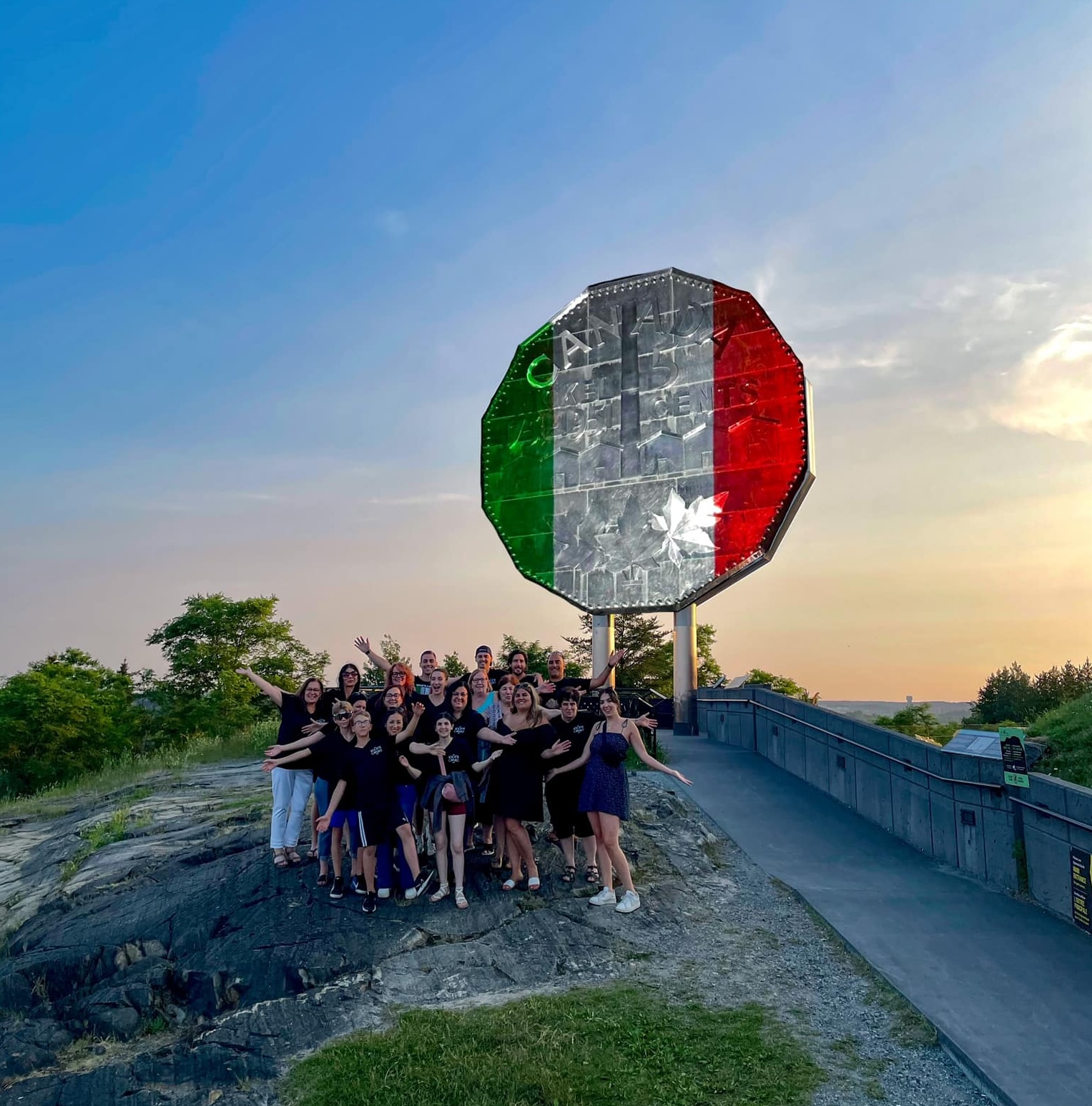The Italian flag projected across the face of the Big Nickel in Sudbury, in front of a darkening blue sky at dusk. 