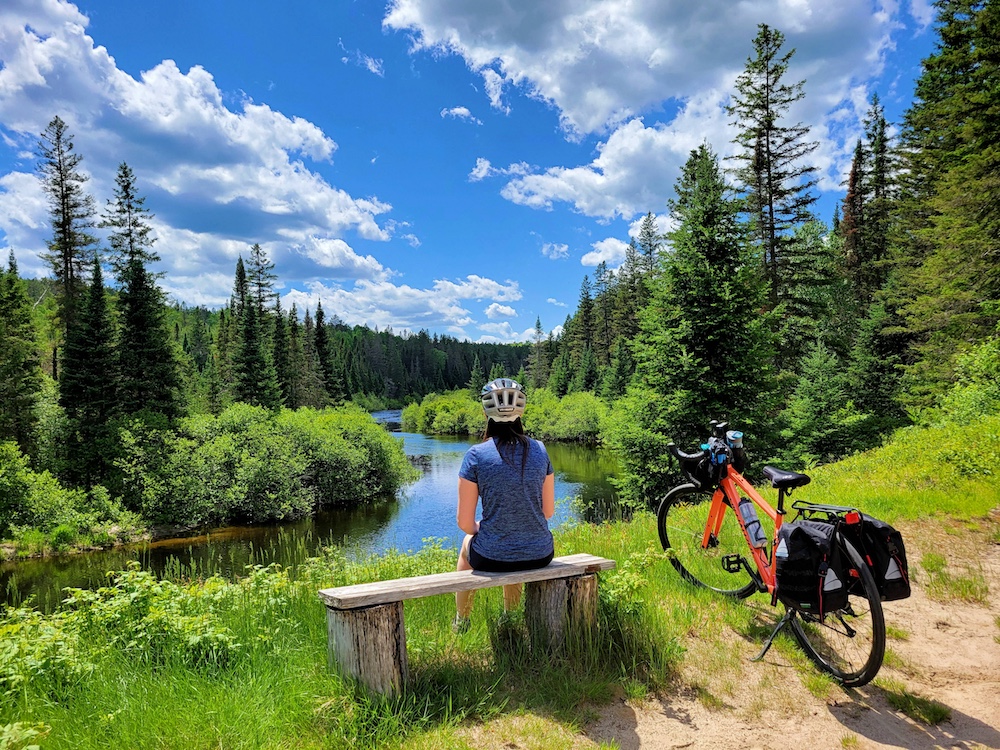 Woman sitting on bench looking out at river with bike beside her