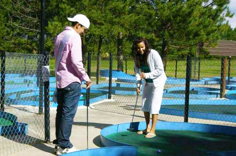 a man and woman happliy play mini golf on a sunny summer day at the Dinosaur Valley Mini Golf course. 
