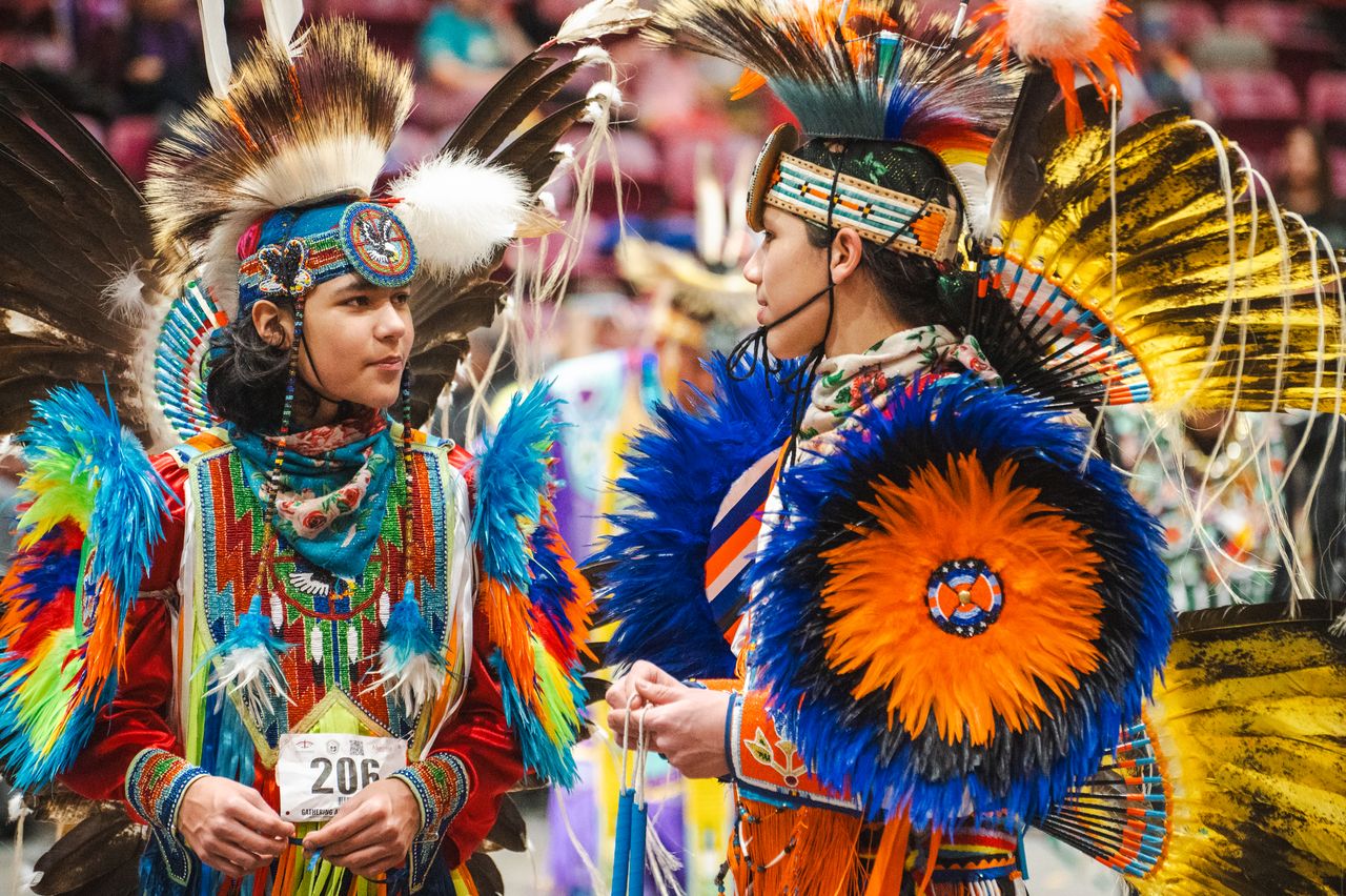 Two dancers at the Gathering at the Rapids pow wow talk happily, dressed in spectacular, brightly-coloured regalia. 