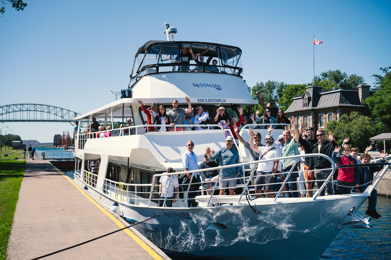 passengers smile and wave from the deck of the Miss Marie tour boat in the Sault Locks on a sunny summer day in Sault Ste. Marie. 