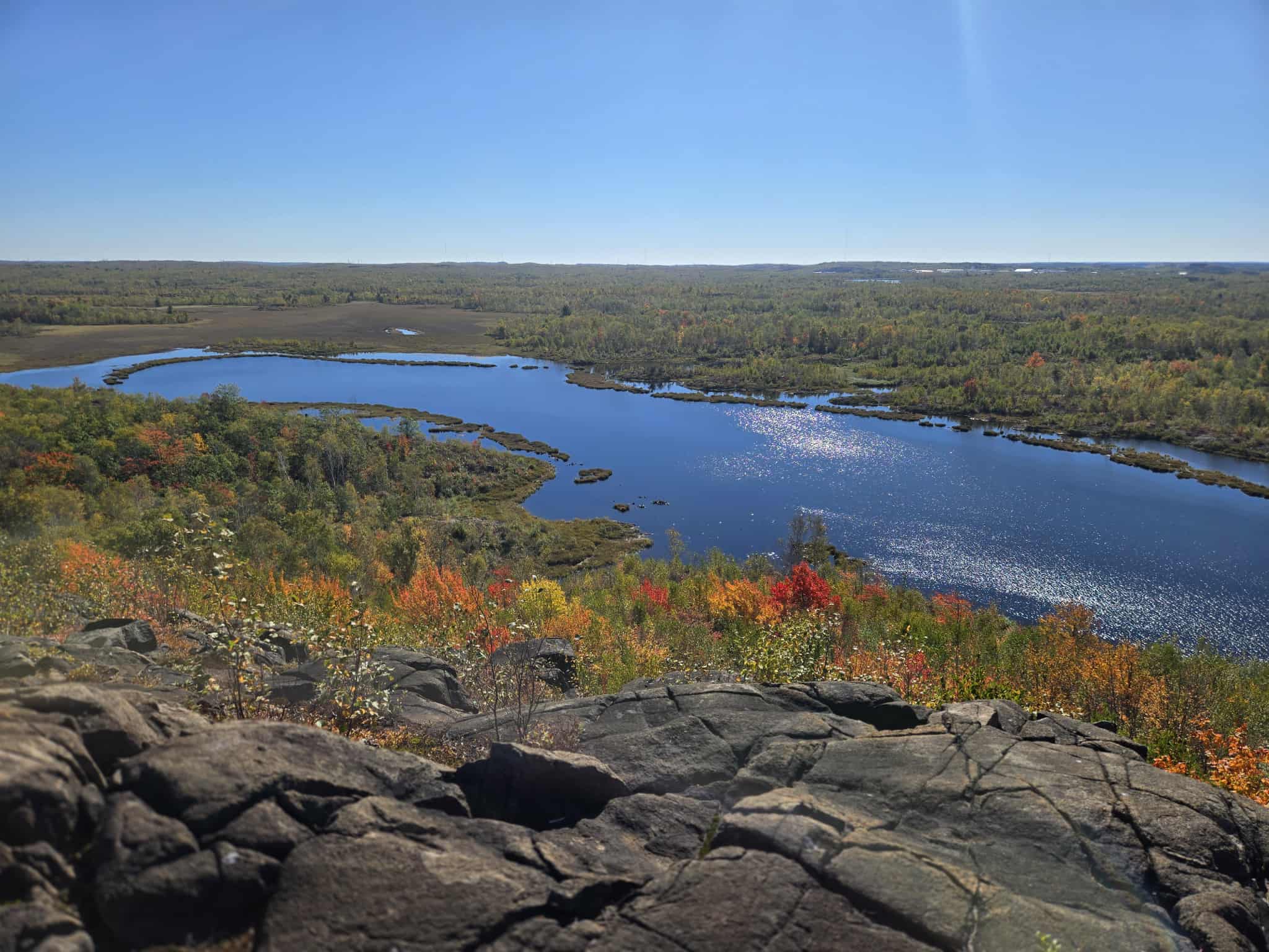 A shining blue river running through a rocky, forested valley below the Voyaguer Trails.