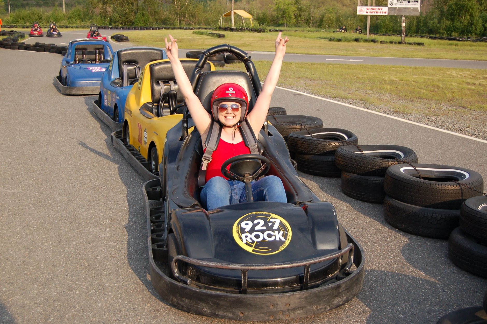 a woman sitting in a go-kart on the Sudbury Kartways track smiles with her arms raised above her head.