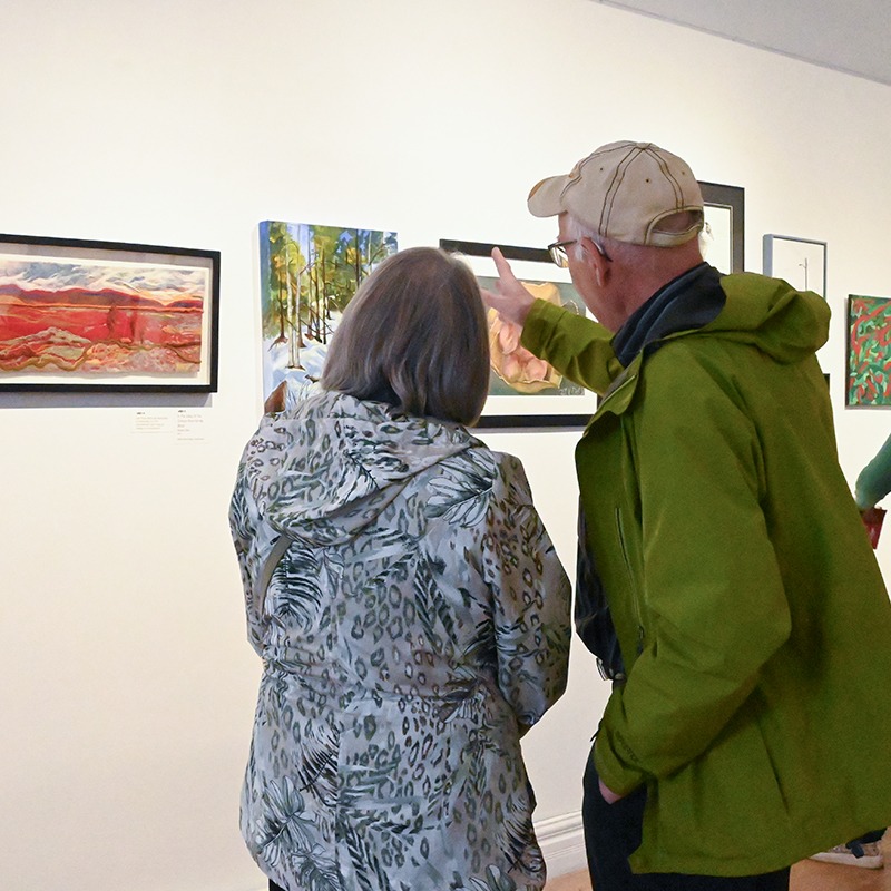 a senior couple stand close together chatting about the art on the gallery wall at the Art Gallery of Sudbury. 