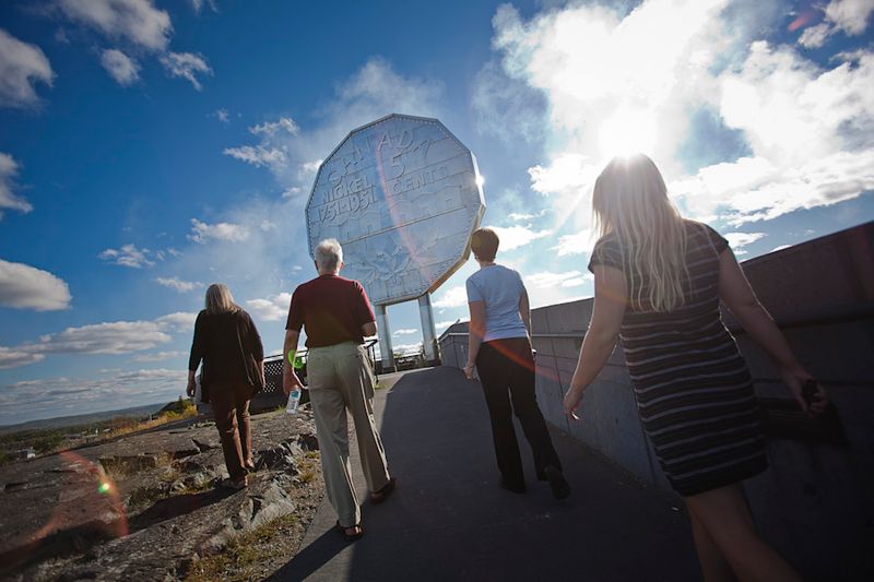 a family group ranging from young adult to senior walk together along the wide smooth paved trails toward the Big Nickel in Sudbury.