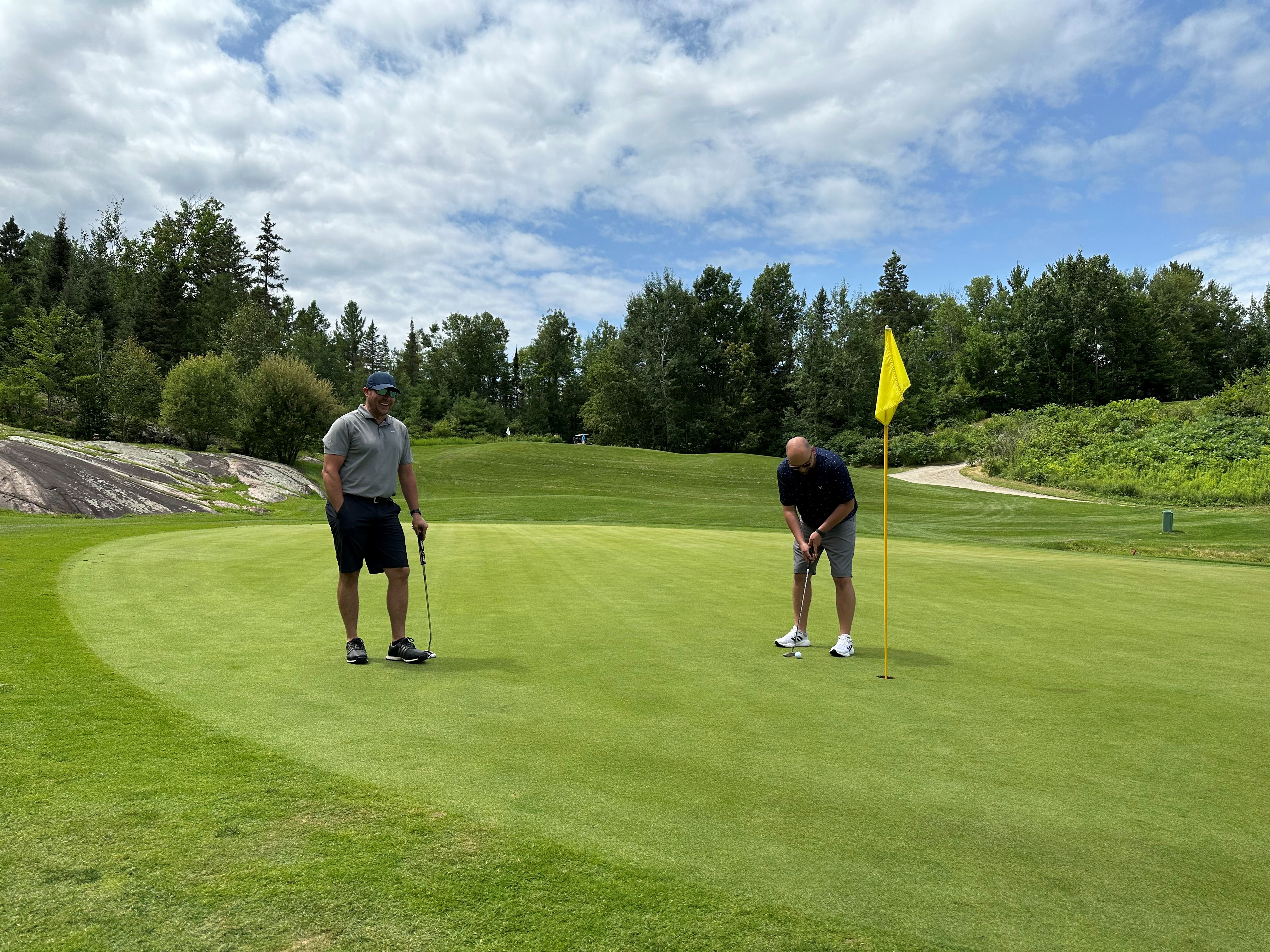 people golfing on a lush, rolling green surrounded by thick trees at the Osprey Golf Course in North Bay. 