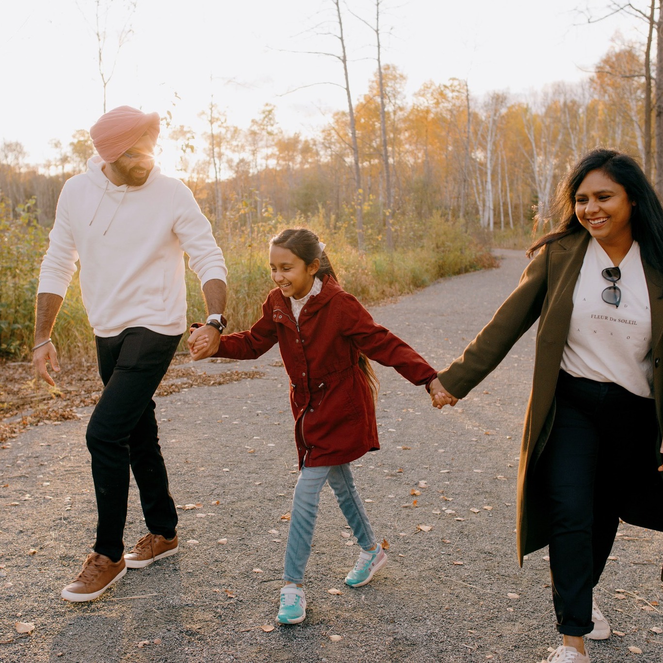 a man, woman and girl smile and hold hands as they stroll along wide smooth Sudbury walking trails at sunset in the autumn. 