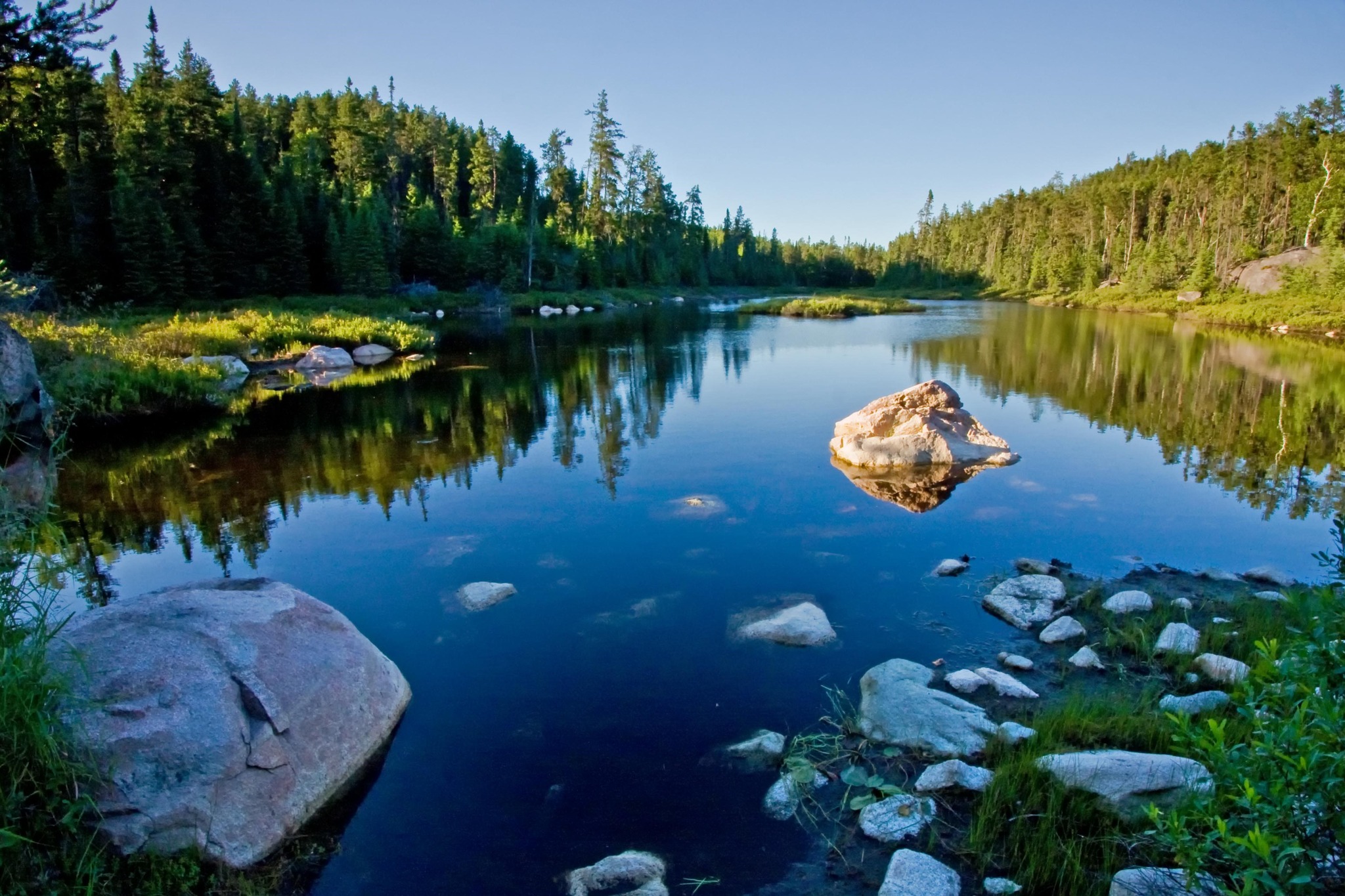 a glassy lake mirroring bright green forest and a cool clear blue sky at Halfway Lake Provincial Park. 
